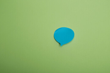 Blue speech bubble paper cutout on bright green background, modern minimal communication concept