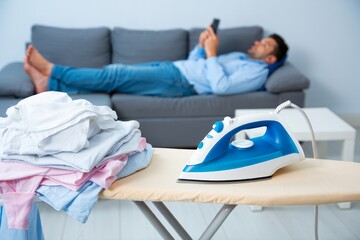 Procrastination and ironing concept man relaxing on couch instead of doing chores