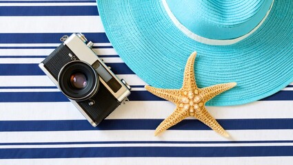 Summer vacation photography concept with camera starfish and blue hat on striped towel