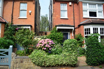 Lush greenery and vibrant flowers create a picturesque garden in front of two charming brick...