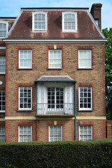 The brick building features a charming balcony and multiple windows, highlighting the architectural style of the area. Lush greenery surrounds the residence, creating a peaceful urban setting