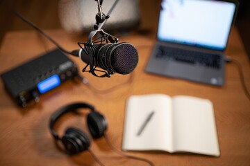 Podcast recording studio setup with microphone headphones laptop and notebook on desk