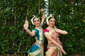 Two beautiful girls dancers in traditional Indian clothes in the park outdoors against the background of greenery in a dance pose