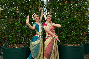 Two beautiful girls dancers in traditional Indian clothes in the park outdoors against the background of greenery in a dance pose