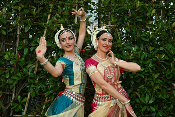 Two beautiful girls dancers in traditional Indian clothes in the park outdoors against the background of greenery in a dance pose