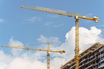 Against the blue sky, two construction cranes are building
