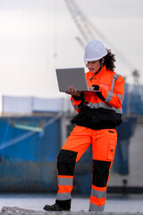 Two port engineers in high-visibility orange uniforms and hard hats communicate while inspecting...