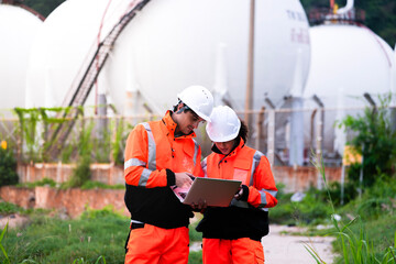 Two engineers in high-visibility safety gear and hard hats discuss project plans on a laptop in...