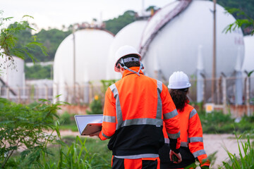 Two engineers in high-visibility safety gear and hard hats discuss project plans on a laptop in...