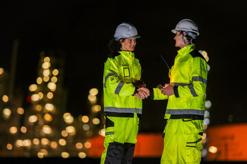 Two night-shift industrial workers in safety gear exchange a cheerful high five, symbolizing...