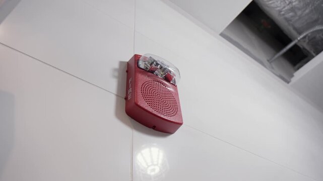 Red fire alarm siren or emergency sounder installed on a white wall in a technical room. Part of safety system.