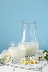 Fresh milk and flowers on white wooden table against light blue background. Dairy product