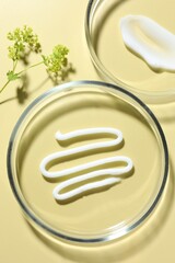 Different cosmetic products in Petri dishes and floral decor on pale yellow background, flat lay