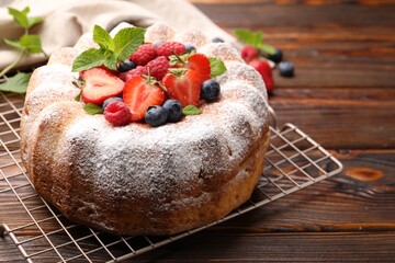 Tasty Bundt cake with powdered sugar and berries on wooden table, closeup. Space for text