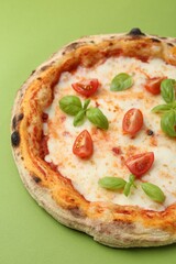 Delicious pizza with tomatoes and basil on green table, closeup