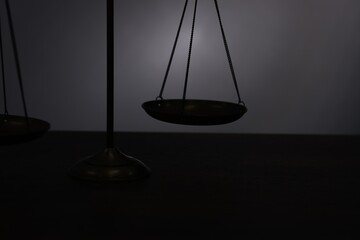 Scales of justice on table in darkness, closeup