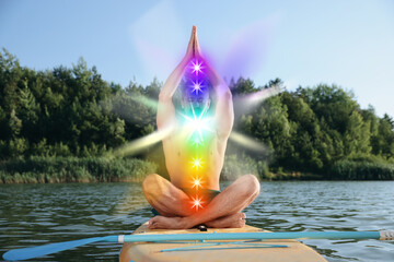 Man meditating in Lotus pose on SUP board. Seven chakras glowing