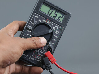Close up male hand on selector digital multimeter on grey background 