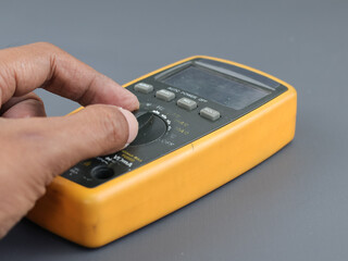 Close up male hand on selector digital multimeter on grey background 