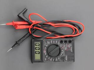 Black digital multimeter with probes for measuring voltage, resistance on grey background, a...