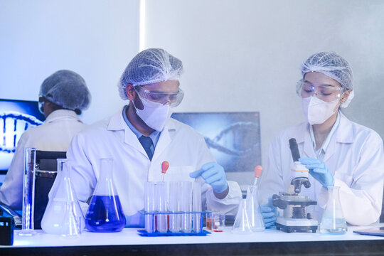 A team of scientists in a biotech lab collaborates on a study. A female researcher looks into a microscope while her male colleague supervises, analyzing samples together.