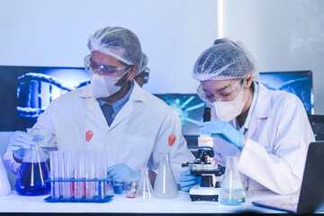 A team of scientists in a biotech lab collaborates on a study. A female researcher looks into a...