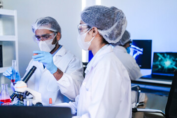 A team of scientists in a biotech lab collaborates on a study. A female researcher looks into a...