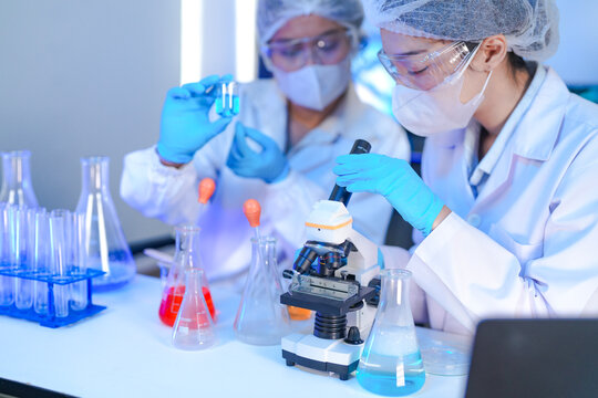 A team of scientists in a biotech lab collaborates on a study. A female researcher looks into a microscope while her male colleague supervises, analyzing samples together.