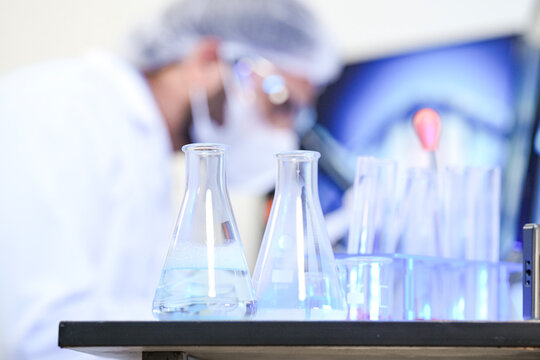 A geneticist in full PPE intently analyzes a sample through a microscope in a modern lab. A DNA double helix on the screen behind him symbolizes research in genetics and biotechnology.