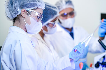 A team of scientists in a modern laboratory meticulously works on an experiment, pipetting a red...