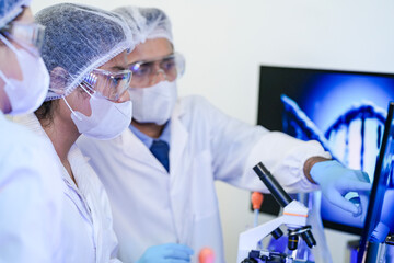 A team of scientists in a modern laboratory meticulously works on an experiment, pipetting a red...
