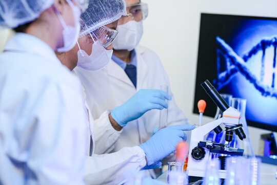 A team of scientists in a modern laboratory meticulously works on an experiment, pipetting a red liquid into a test tube next to a microscope, focused on medical research and analysis.