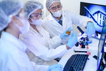 A team of scientists in a modern laboratory meticulously works on an experiment, pipetting a red...
