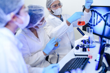 A team of scientists in a modern laboratory meticulously works on an experiment, pipetting a red...