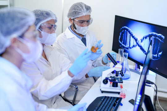 A team of scientists in a modern laboratory meticulously works on an experiment, pipetting a red liquid into a test tube next to a microscope, focused on medical research and analysis.