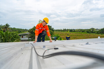 Technician in safety uniform and helmet kneeling on a rooftop, using a drill for precise...