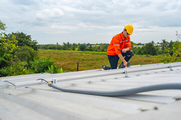 Technician in safety uniform and helmet kneeling on a rooftop, using a drill for precise...
