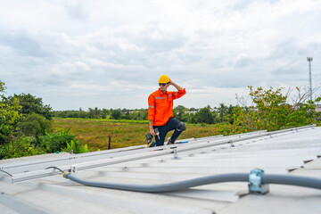 Obraz premium Technician in safety uniform and helmet kneeling on a rooftop, using a drill for precise installation work. A scene highlighting safety, professionalism, and technical expertise in construction.