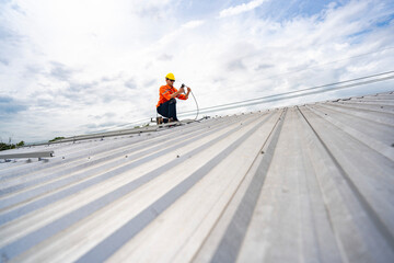 Technician in safety uniform and helmet kneeling on a rooftop, using a drill for precise...
