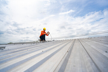 Technician in safety uniform and helmet kneeling on a rooftop, using a drill for precise...