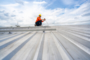 Technician in safety uniform and helmet kneeling on a rooftop, using a drill for precise...