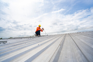 Technician in safety uniform and helmet kneeling on a rooftop, using a drill for precise...