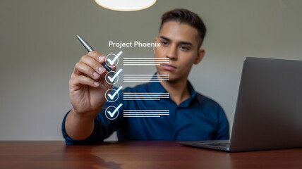 Young man checking off tasks on a digital checklist with a pen next to a laptop to do list task management