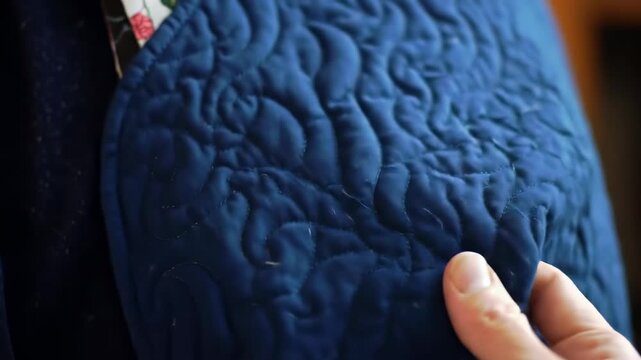 Close-up of a dark blue quilted fabric.  Hands examining it