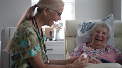 A nurse happily engages with an elderly woman while reviewing her medications, creating a warm atmosphere in a senior living facility during a routine visit.