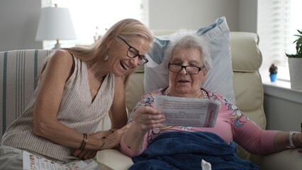 In a cozy senior living facility, a daughter and her elderly mother smile together as they share cherished memories from a photo album, creating moments of joy.