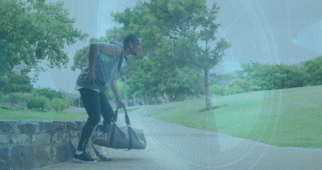 Lifting duffel bag, African American man wearing hoodie and leggings beside park bench, copy space