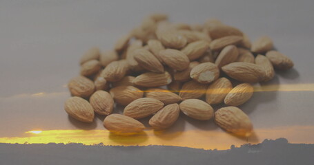 Displaying heap of tan whole almonds reflecting on smooth tabletop, with sunset hill silhouette