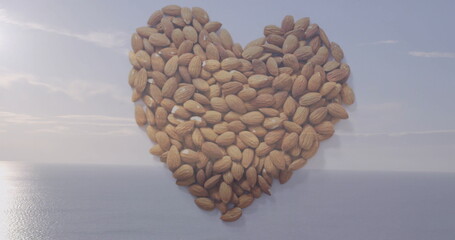 Heart-shaped cluster of whole almonds resting on shore at coastal vista, with calm ocean reflection