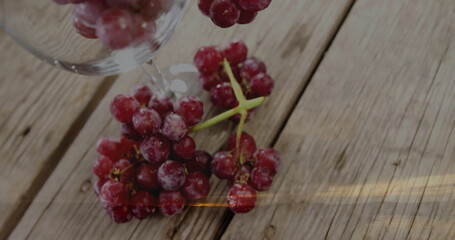 Showing frosted red grapes resting on rustic wooden tabletop, under inverted clear wine glass